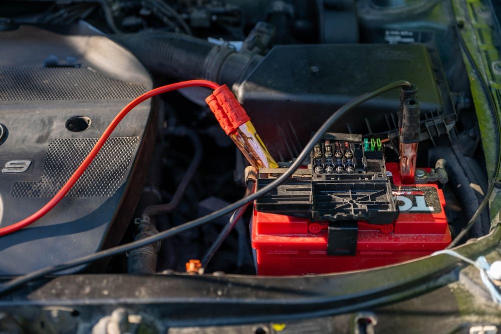 Car battery with red jumper cables connected in an engine bay