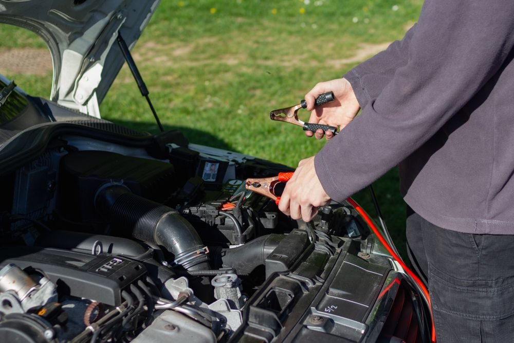 Mechanic using jumper cables to jump-start a car battery outdoors